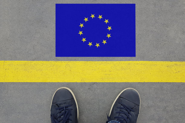 从一条柏油路开始，上面有欧盟国旗，脚上穿着鞋子。欧盟概念下的移民和旅游图片下载