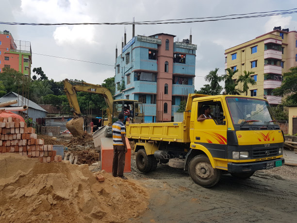 2024年8月5日，孟加拉国达卡。这张照片显示了街道上的一辆卡车，它的驾驶室是黄色的，侧面有一条红色的条纹。卡车停在一栋在建建筑附近。图片下载