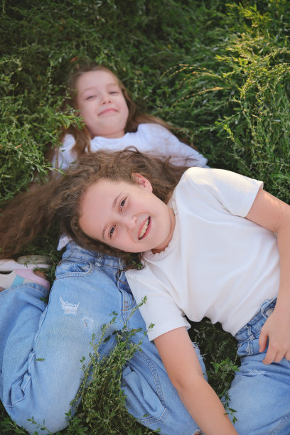 俯视图，两个快乐微笑的孩子躺在绿色的草地上。开朗的两姐妹一起笑。图片下载