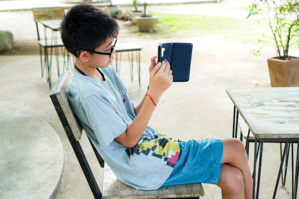一个男孩在户外餐桌上放松时使用智能手机应用的照片。图片下载