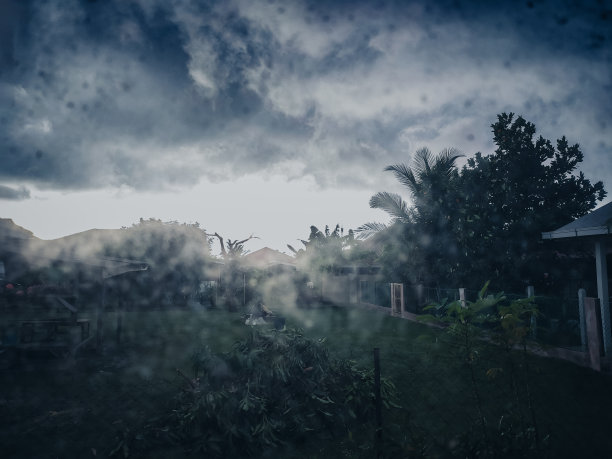 这张照片是在大雨季节从房子里拍摄的，展示了窗户上的露珠，创造了一个美丽的、雾蒙蒙的雨季外面的景色。马来西亚关丹省下大雨图片下载