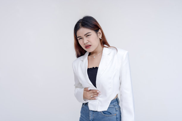 一个生病的年轻女子抱着肚子痛，抱着肚子不舒服。孤立在白色背景上。图片下载