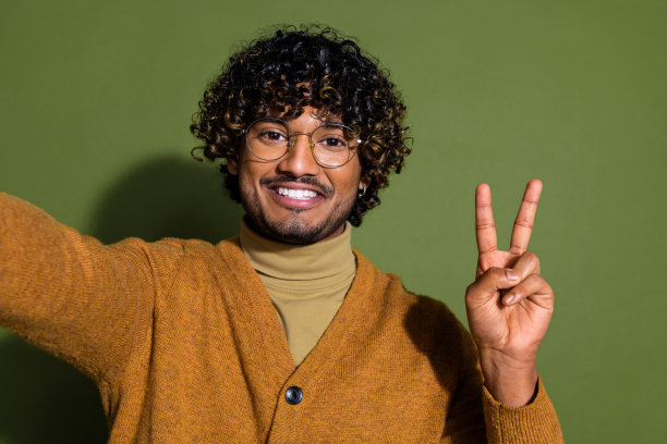 漂亮的年轻男性自拍照片v字穿着时髦的棕色衣服孤立在卡其色背景图片下载