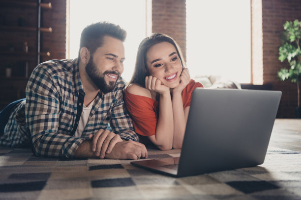 吸引人的欢快躺在地板上的照片上网本电子商务已婚的年轻夫妇花空闲时间搬新公寓，家庭室内室内图片下载