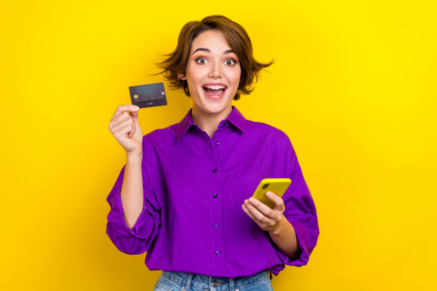 照片中漂亮的年轻女孩手持信用卡设备，穿着时尚的紫色智能休闲服装，孤立在黄色背景上图片下载