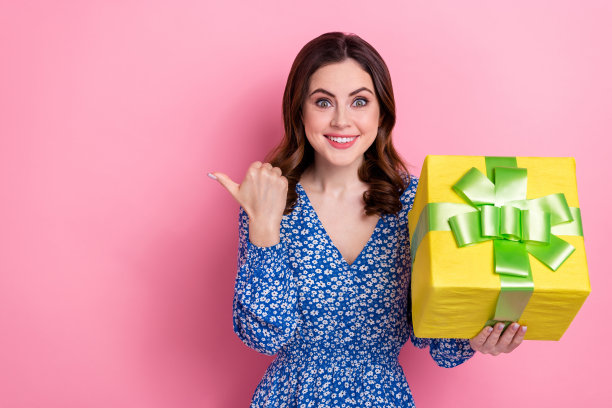 印象深刻的女人的照片，波浪发型，穿着蓝色的衣服，拿着礼物盒，直接在粉红色的背景上购物图片下载