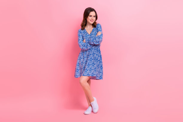 全尺寸照片的友好积极可爱的女孩穿蓝色的衣服，白色的运动鞋站立双臂交叉孤立在粉红色的背景图片下载