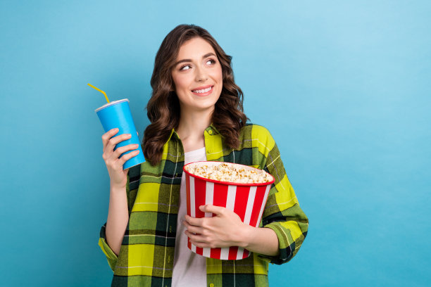 梦幻可爱的女士穿着格子夹克吃爆米花喝百事可乐空的空间孤立的蓝色背景的照片图片下载