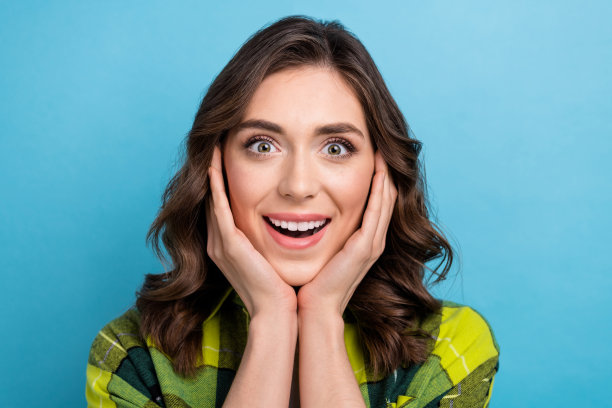 照片中兴奋时髦的女人穿着格子衬衫微笑的手臂脸颊孤立的蓝色背景图片下载