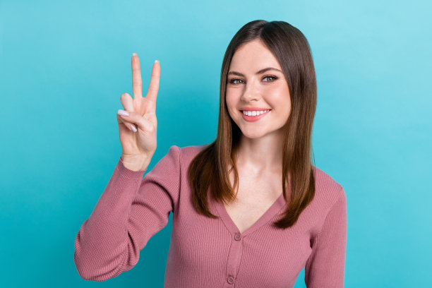 年轻女孩的照片穿着粉红色的衬衫，显示v字形友好的符号问候所有脸书个人资料头像隔离在蓝色背景图片下载