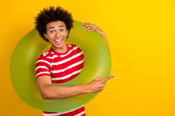 照片上积极兴奋的家伙穿着条纹t恤指着空旷的空间，拿着漂浮的戒指孤立的黄色背景图片下载