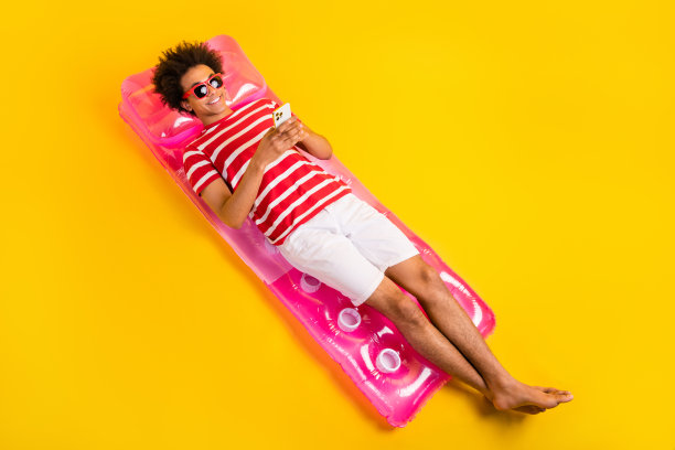 全身照片开朗的酷男人穿着红色t恤躺在漂浮床垫聊天装置孤立的黄色背景图片下载