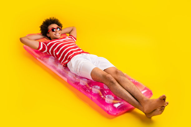 漂亮梦幻的男人穿条纹t恤放松充气床垫的全长照片孤立的黄色背景图片下载