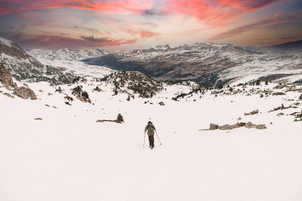 孤独的滑雪者走在积雪的草地上，背景是美丽的山景图片下载