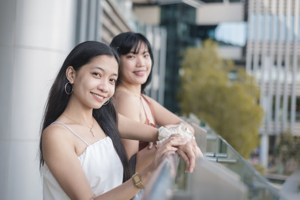 两个亚洲女人微笑着在露天商场的窗台边闲逛的照片。图片下载