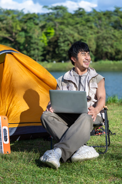 年轻的亚洲人在露营地用笔记本电脑工作，用太阳能电池板，享受在大自然中远程工作图片下载