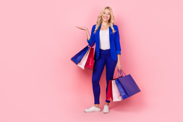 照片迷人的专业女士拿着商店的袋子，举起手掌，价格低廉，提供促销孤立的粉红色背景图片下载