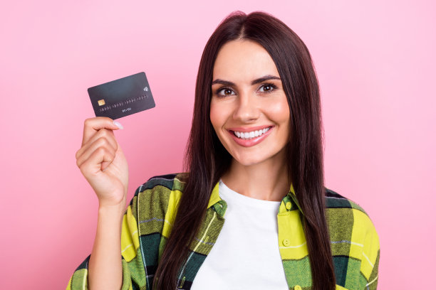 照片中的女孩心情很好，直发，穿着格子衬衫，拿着塑料卡片，孤立在粉红色的背景上图片下载