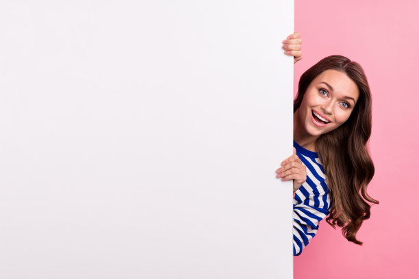 照片的兴奋时髦的女孩躲在巨大的白板横幅新奇的好消息促销商店广告孤立在粉红色的背景图片下载