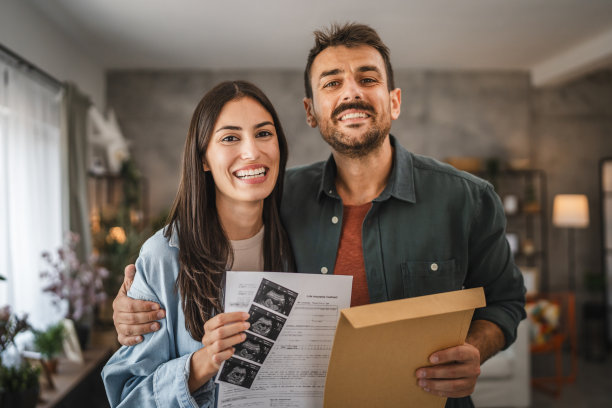 成年夫妇站着，拿着婴儿和信封的超声波照片图片下载