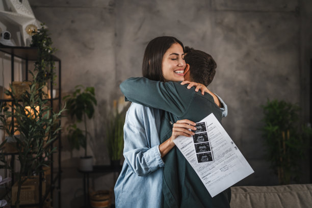 情绪激动的夫妇互相拥抱，拿着婴儿的超声波照片图片下载