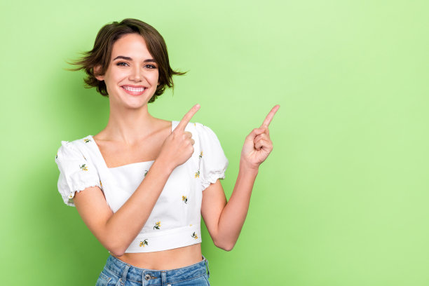 照片上漂亮漂亮的女孩直接手指空白的空间广告牌上穿着时尚的短上衣孤立的淡绿色背景图片下载