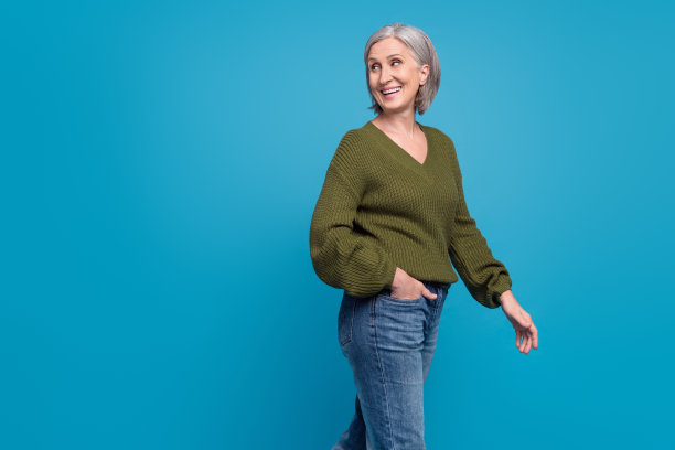 迷人的开朗的高级妇女的照片广告服装收集牛仔裤裤子卡其色毛衣使步骤孤立的蓝色背景图片下载