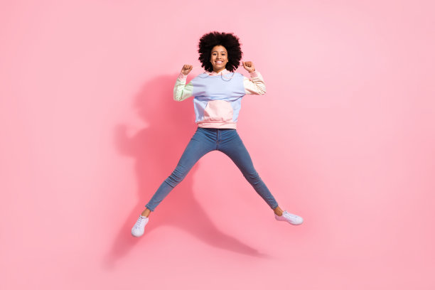 全身照片闪亮的幸运小孩穿运动衫上升的拳头跳跃高孤立的粉红色背景图片下载