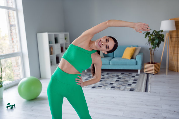 照片中，微笑的迷人的年轻女孩穿着运动服在家里做早操图片下载