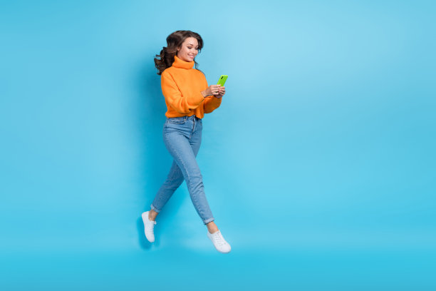 全身照片开朗闪亮的女人穿橙色毛衣跳聊天装置空的空间孤立的蓝色背景图片下载