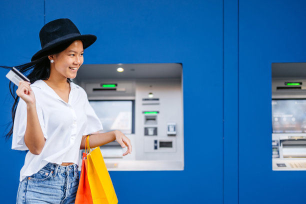 在西班牙巴塞罗那，一名年轻的亚洲女子拎着购物袋在自动取款机前用信用卡取钱图片下载