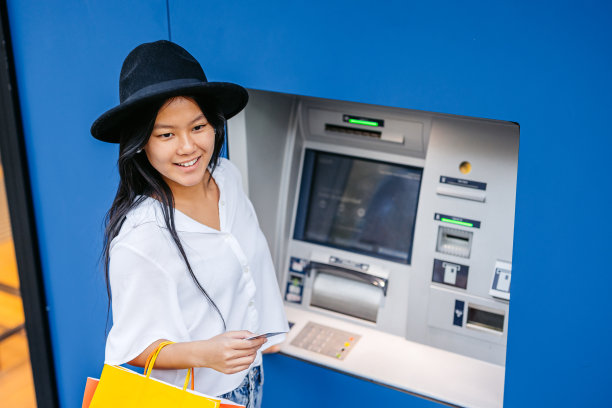 在西班牙巴塞罗那，一名年轻的亚洲女子拎着购物袋在自动取款机前用信用卡取钱图片下载