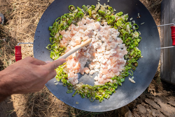 在大自然中，男性用手在煤火上用锅子把烤过的蔬菜和鸡肉混合在一起烹饪。人类的汉图片下载