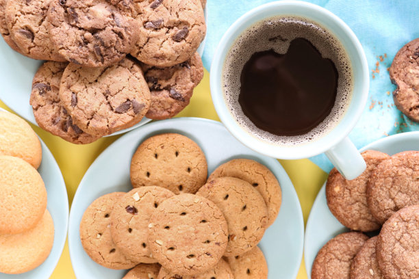 全画幅图片，盘子里是新鲜出炉的自制混合各种饼干，周围是满满的，蓝色的黑咖啡杯，双层巧克力饼干，巧克力饼干，全麦饼干和酥饼圆，黄色背景，高架视图图片下载