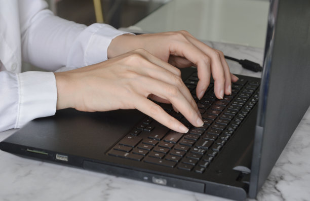 女性办公室职员的手在黑色笔记本电脑上打字的特写照片。图片下载