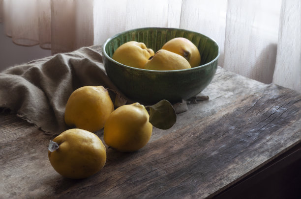 一个美丽的静物照片，新鲜采摘的榅桲在一个手工制作的绿色陶瓷碗，在一个饱经风霜的木板前图片下载