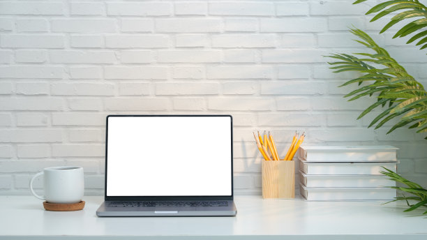 极简主义的家庭办公室设置展示了一个光滑的笔记本电脑与一个空白的白色屏幕，完美的添加自己的内容。工作空间的特点是干净。图片下载