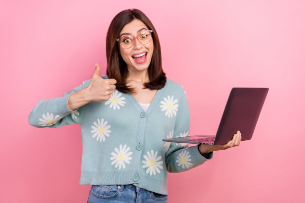 照片兴奋的年轻女孩棕色头发穿花印刷开衫率看netflix笔记本电脑没有广告孤立在粉红色的背景图片下载