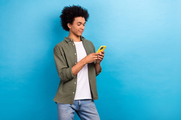 年轻专注的博主男子拿着智能手机写推特演讲的照片，穿着蓝色背景的时尚服装图片下载