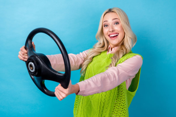 年轻时髦的女孩的照片金发波浪的头发握住方向盘驾驶她的第一辆汽车买保险孤立的蓝色背景图片下载