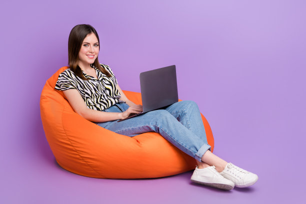 全长肖像正面华丽的人坐在舒适的包使用上网本孤立的紫色背景图片下载