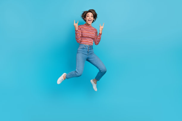时髦的酷女人穿着印花上衣跳高显示硬岩石标志空的空间孤立的蓝色背景的全身照片图片下载