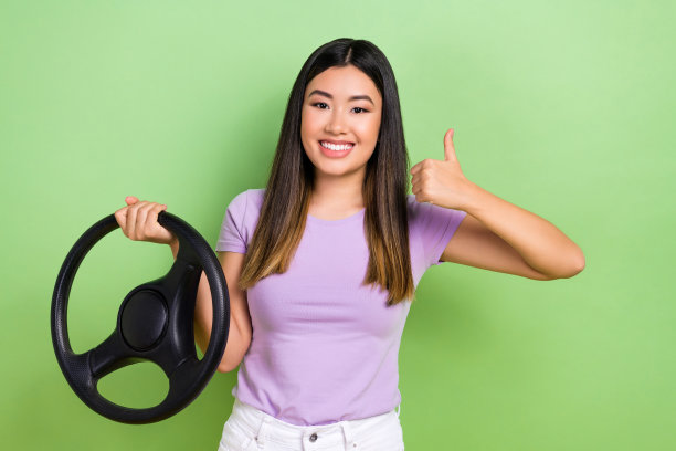 积极的年轻越南女孩的照片大拇指向上推荐购买保时捷汽车方向盘孤立的绿色背景图片下载