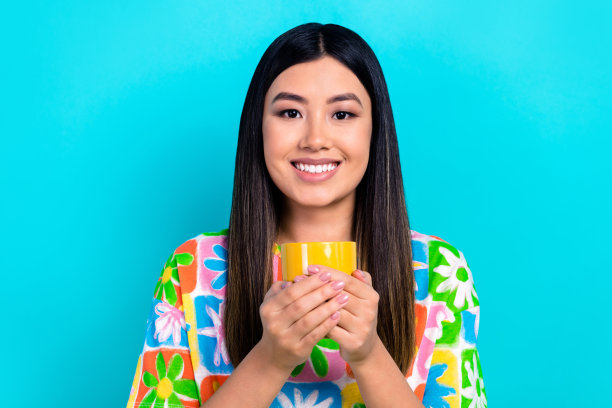 照片的开朗甜美的女人穿着印花t恤享受美味的饮料孤立的蓝色背景图片下载