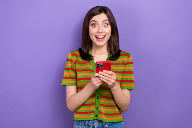 照片中，一位无言以对的女子直发，穿着彩色t恤，在紫色背景下用智能手机阅读新闻图片下载