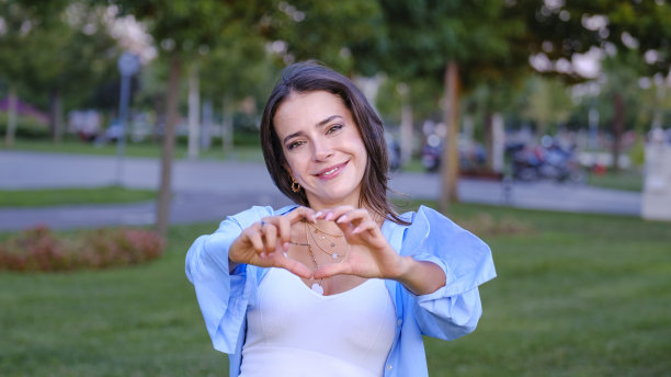 一个年轻漂亮的女商人在公园里看着镜头用手做了一个心形图片下载