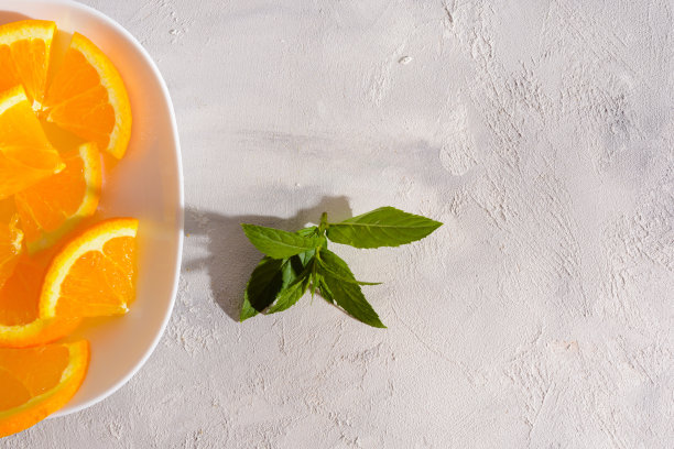 一张白色盘子的特写照片，白色的背景上放着橘子片和一小枝薄荷叶图片下载