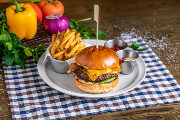 啤酒汉堡，有牛肉、薯条、番茄酱、蛋黄酱、西红柿、洋葱、辣椒、香菜，装在餐巾纸上的盘子里，木质桌子上的意大利快餐侧视图图片下载