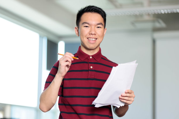 一位身穿条纹衬衫的年轻男大学生拿着纸和铅笔图片下载