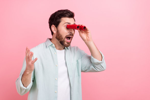 照片中，疯狂的年轻人拿着老式的双筒望远镜看着空旷的空间，在粉红色的背景上孤立地表演戏剧图片下载
